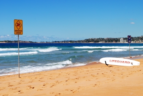 Warning sign and lifeguard surfboard on a beach in Sydney - Australian Stock Image