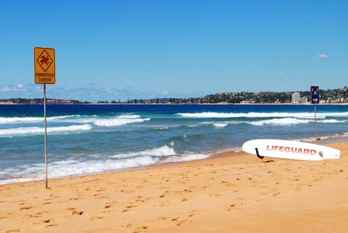 Warning sign and lifeguard surfboard on a beach in Sydney