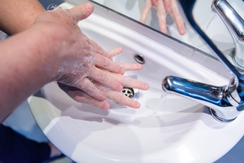 Washing hands with soap and water at basin - Australian Stock Image