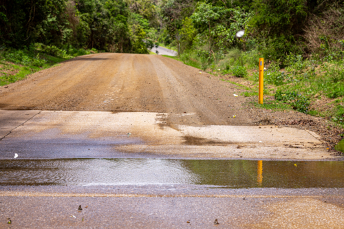 Water over flooded floodway on gravel road - Australian Stock Image