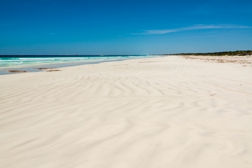 wave patterns on a white sand beach leading to a far horizon and dark blue sky - Australian Stock Image