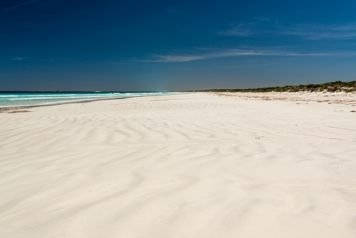 Wave patterns on a white sand beach leading to a far horizon and dark polarised blue sky - Australian Stock Image
