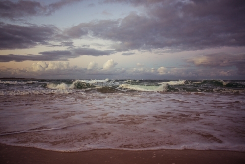 Waves crashing on the beach under a brooding sky - Australian Stock Image