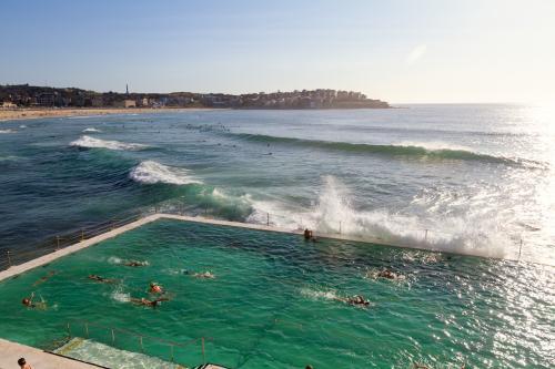 Waves crashing over Bondi Baths at sunrise with people swimming laps