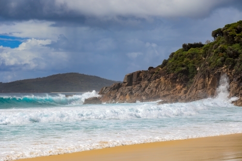 Waves crashing over rocky coastline against cloudy sky - Australian Stock Image