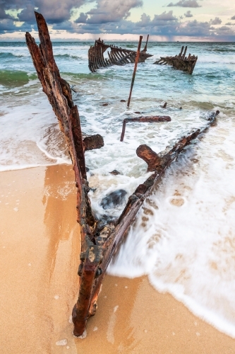 Waves engulfing the bow of a shipwreck on a beach