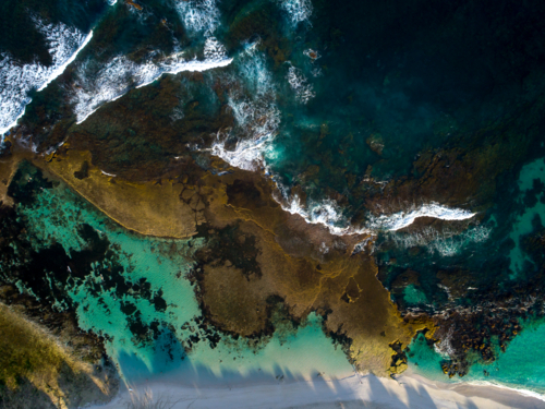 Waves flock to the shore over an exposed reef - Australian Stock Image