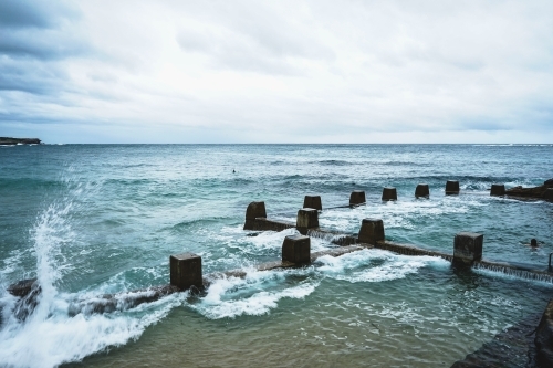 Waves splashing against ocean rock pool in Coogee Sydney on a cloudy day - Australian Stock Image