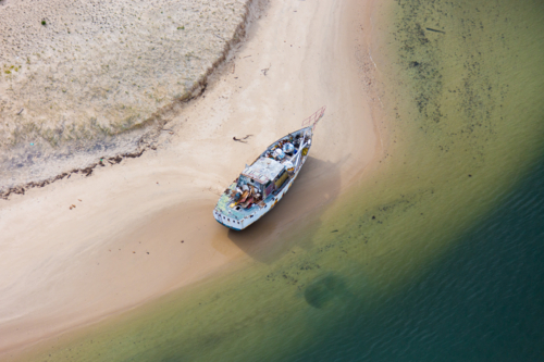 Weathered abandoned boat stranded on sandy shoreline with shallow water - Australian Stock Image