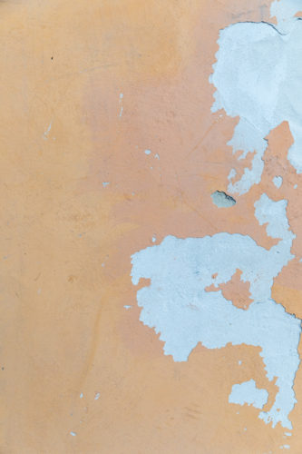 Weathered ochre coloured rendered wall with blue paint chips - Australian Stock Image