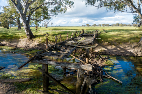 Weathered timber bridge collapsing over a quiet country creek - Australian Stock Image