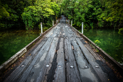 Weathered timber bridge over calm green water - Australian Stock Image