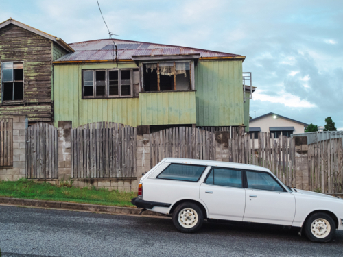 Weathered two‑storey house with station wagon outside - Australian Stock Image