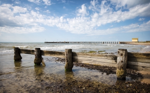 weathered wooden groyne with pier and shed in background