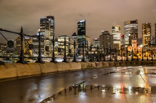Wet Circular Quay at night after the rain with reflections of buildings along the foreshore path.