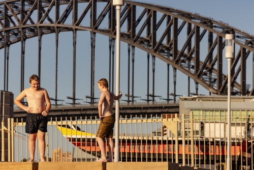 Wet kids jumping standing on ledge at Marrinawi Cove with Sydney Harbour Bridge in background - Australian Stock Image
