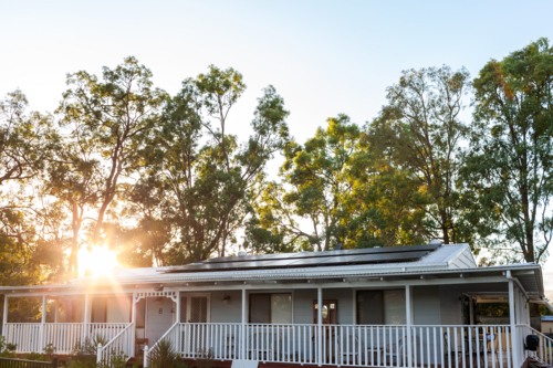 White country cottage with solar panels installed on tin roof with gum trees behind at sunrise - Australian Stock Image