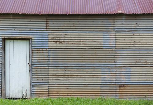 White door set in rusty wall of corrugated iron shed
