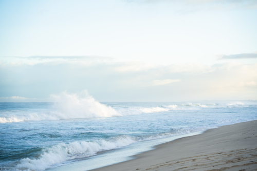 White foamy ocean waves rolling onto sandy shore, cloudy blue sky at Scarborough Beach, Perth - Australian Stock Image