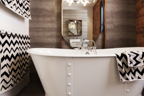 White free standing vintage style bath tub with chevron pattern black and white towels - Australian Stock Image