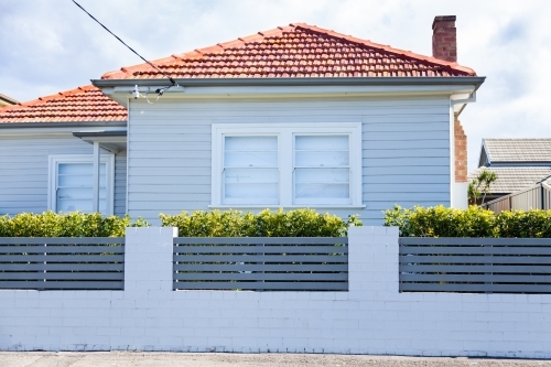 White house with red tiled roof on street, white brick fence - Australian Stock Image