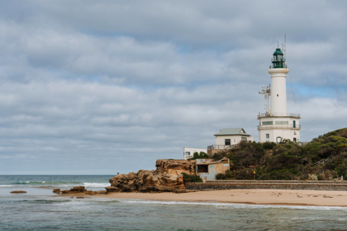 White lighthouse stands on a rocky headland overlooking the ocean - Australian Stock Image