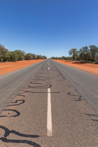 White lines down the middle of the road in Outback NSW with red dirt edges