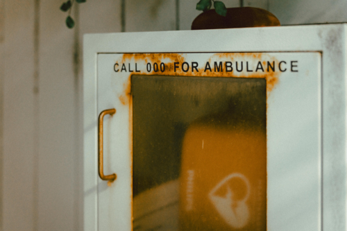 White metal cabinet mounted on a wall, labelled clearly with the text “CALL 000 FOR AMBULANCE” - Australian Stock Image