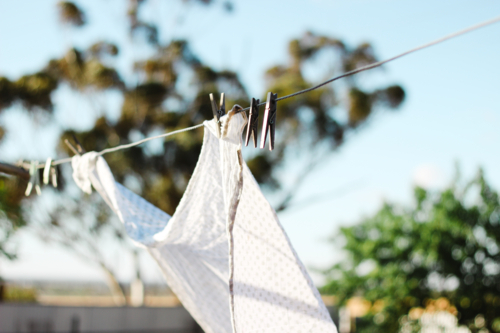 White patterned fabric clipped into the clothesline with wooden clothespins under the sunlight - Australian Stock Image