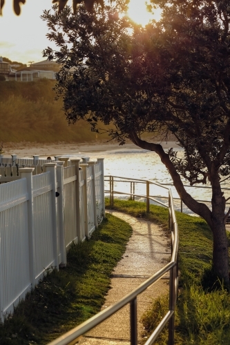 White picket fence by the sea bathed in golden afternoon sunlight - Australian Stock Image