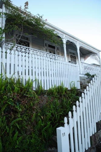 White picket fence in front of a house with a porch. - Australian Stock Image