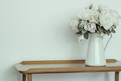 White Roses in a white vase on a timber hallway table inside a country home - Australian Stock Image