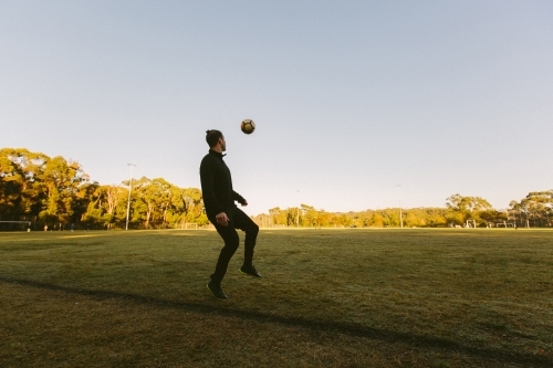Whole body shot of a young man on the field kicking a ball in the air - Australian Stock Image