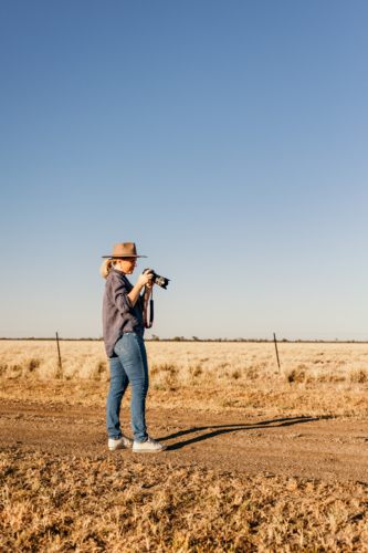 Wide angle of female holding camera in paddock - Australian Stock Image