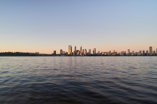 Wide angle view of the Perth city skyline at dusk across the water of the Swan River.