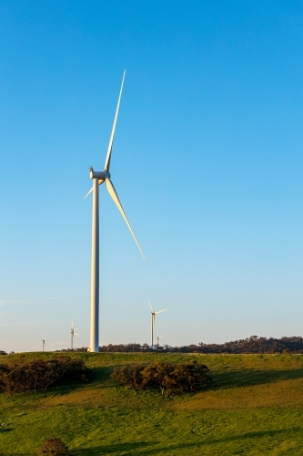 wind turbine on hill top with farmland in foreground, vertical - Australian Stock Image