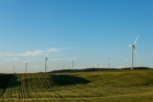 wind turbines on hill tops with farmland in foreground - Australian Stock Image