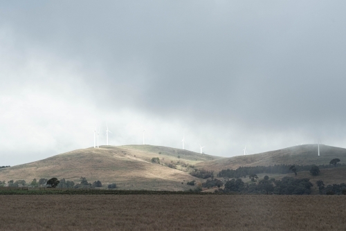 wind turbines on the hilly horizon with low lying cloud - Australian Stock Image