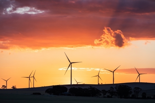 wind turbines silhouetted against orange sunset - Australian Stock Image