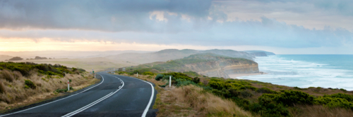 Winding coastal road overlooking cliffs and ocean under a dramatic morning sky. - Australian Stock Image