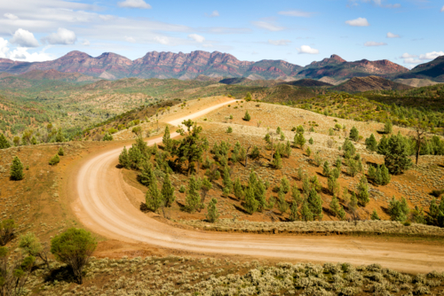 Winding dirt road through the Flinders Ranges beneath rugged mountain peaks - Australian Stock Image