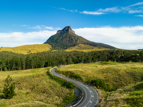 Winding Road leading towards steep rocky mountain - Australian Stock Image
