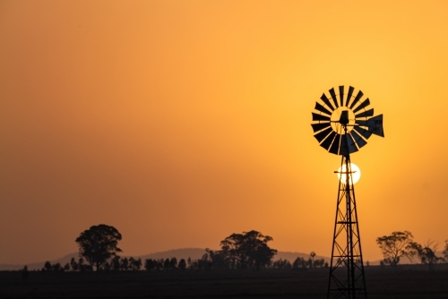 Windmill against a smoky sunset in drought conditions - Australian Stock Image