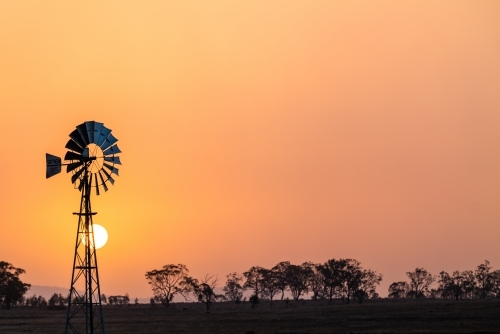 Windmill against a smoky sunset in drought conditions - Australian Stock Image