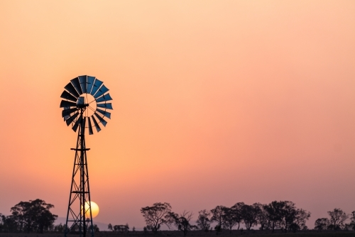 Windmill against a smoky sunset in drought conditions - Australian Stock Image