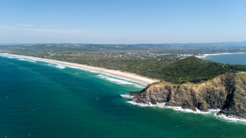 Windswept headland above rugged coastline with steep cliffs with long stretch of white sand beach - Australian Stock Image