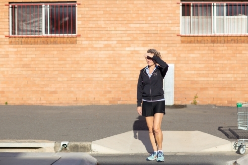 Woman about to cross the road in front of a brick building - Australian Stock Image
