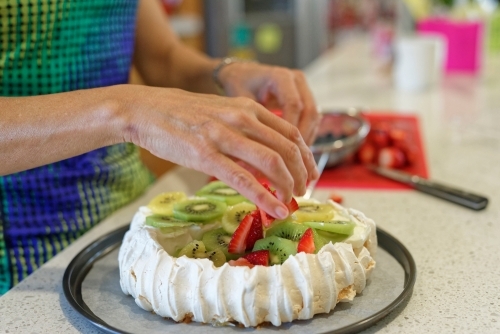 Woman adding fruit on top of the traditional Australian Pavlova - Australian Stock Image