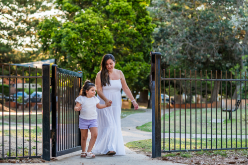 Woman and girl walk together through gate in park on a sunny day - Australian Stock Image
