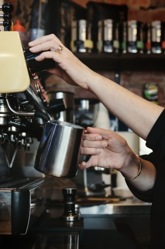 Woman barista making espresso coffee and frothing milk with steam - Australian Stock Image